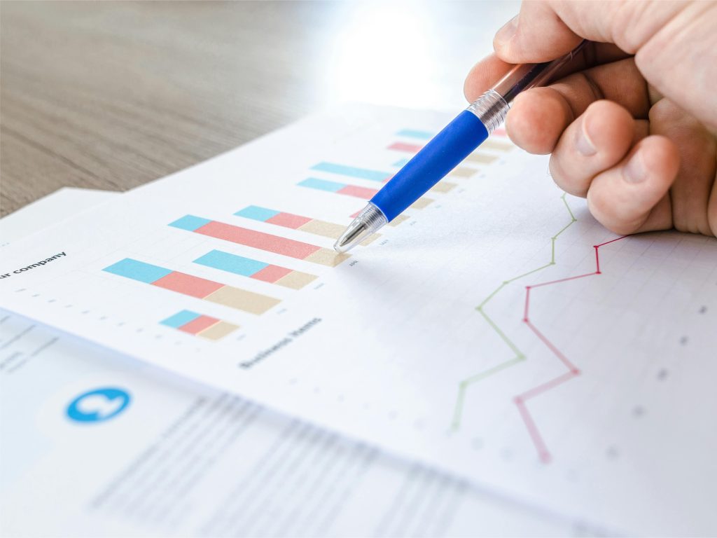 Hand-pointing-at-business-charts-and-growth-analytics-on-paper-with-a-blue-pen
