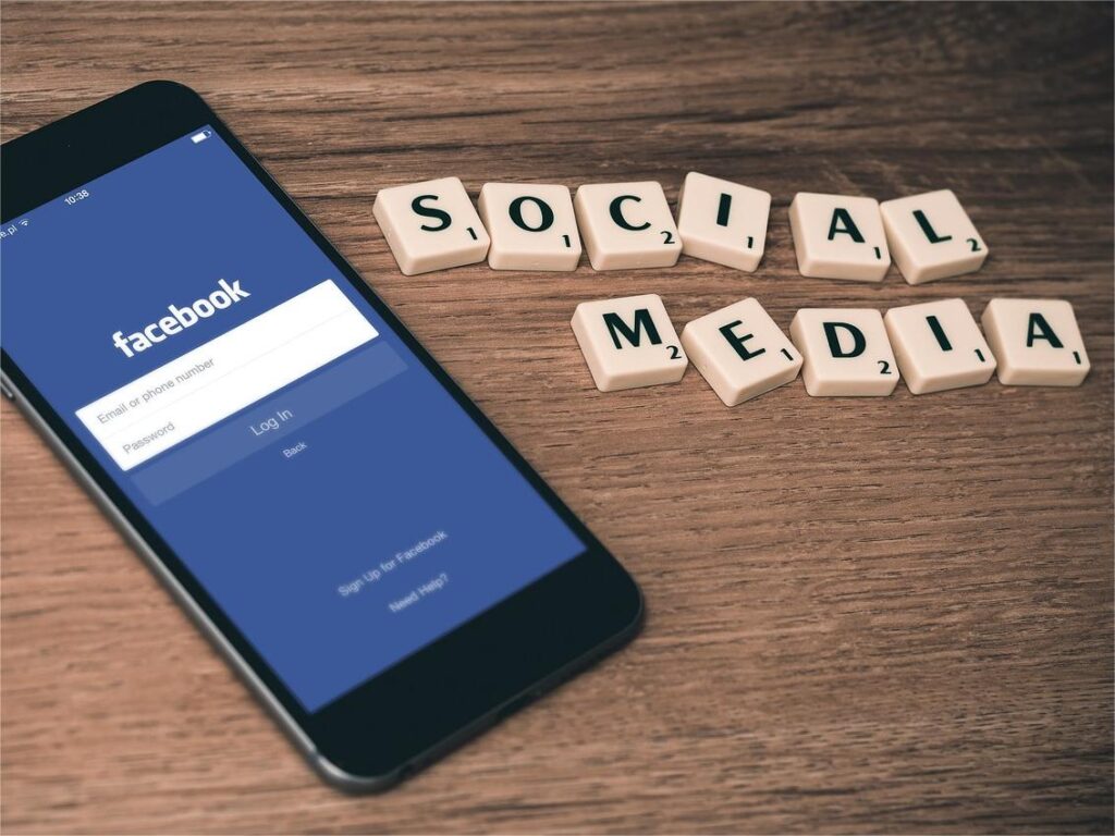 Smartphone-displaying-Facebook-login-screen-next-to-Scrabble-tiles-spelling-Social Media-on-wooden-table